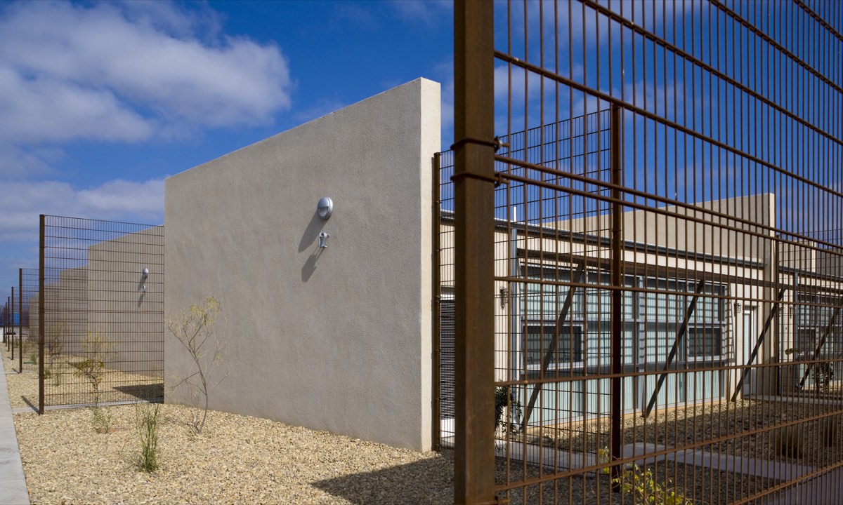 Stucco homes with steel privacy screens and gravel yards under a blue sky at Lo Lomas, Clovis NM